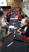 Long table with the following people (front to back) talking one-to-one across from each other: Carrie Banks with Leslie Heinzler, Neil Bernstein (caught smiling at the camera) with Michael Lang, Eric Hone with Karen Keninger (hard to see who this is exactly) and Kim Charlson, Chris Boynton with Annette Teows, Maggie Ansty with Michelle Wisniewski, can't make out the people at the end.